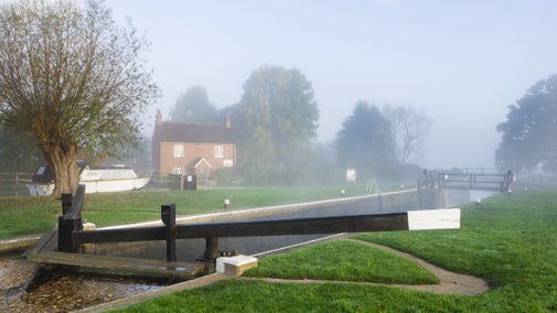 Lock gates in the foreground with a lock keeper's cottage behind on a misty autumnal morning